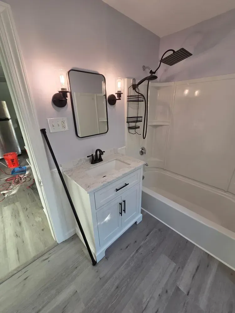 Small bathroom with white vanity, mirror, wall sconces, and a tub/shower with black fixtures.