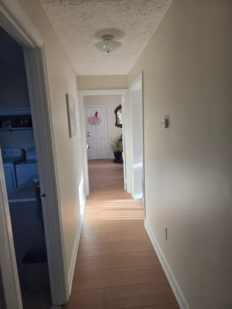 Narrow hallway with wood floor, open doorways, and daylight at the far end