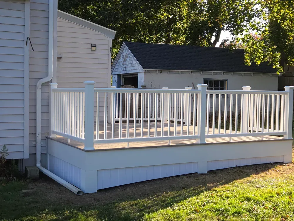 White deck with railings attached to a light-colored house in a sunny backyard