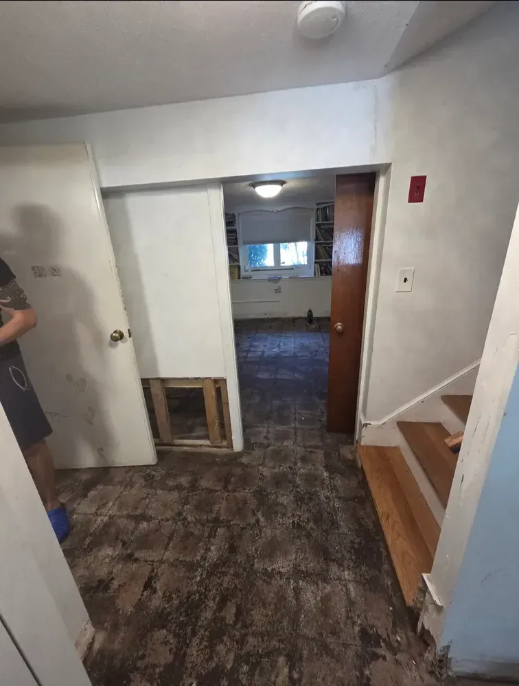 Small hallway with worn flooring, white walls, a doorway to another room, and a staircase on the right.