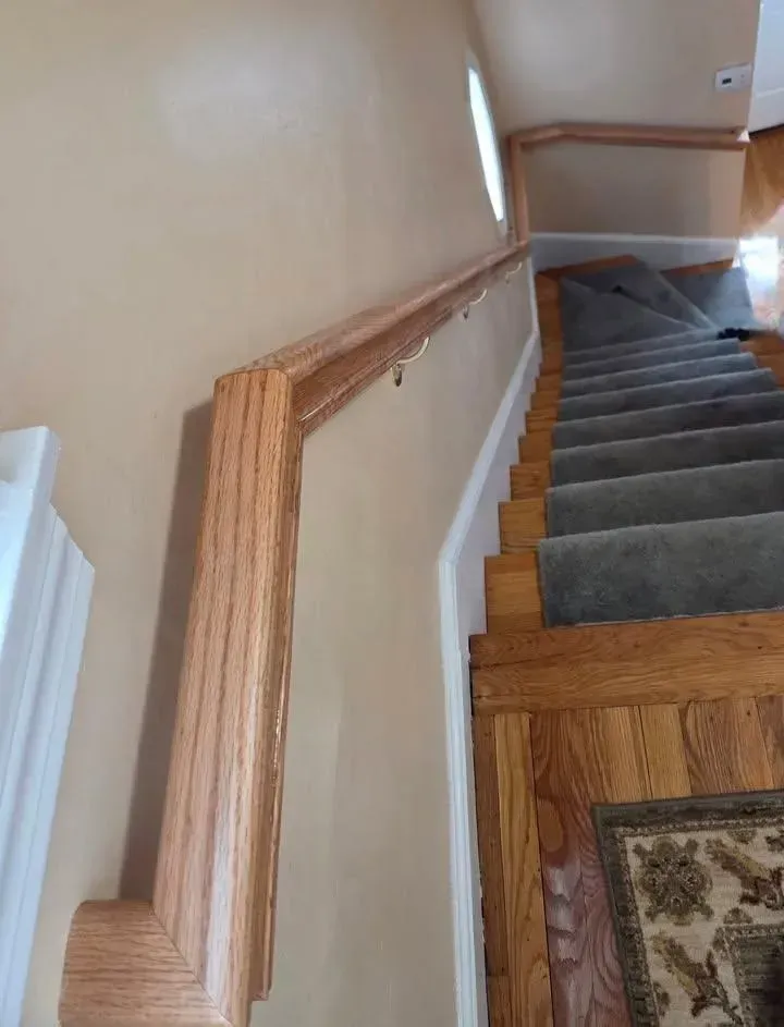 Staircase with gray carpet runner, wood flooring, and beige walls, viewed from the landing.