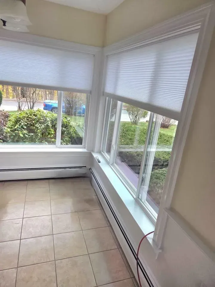 Sunlit enclosed porch with tiled floor, large windows, and white blinds overlooking a garden