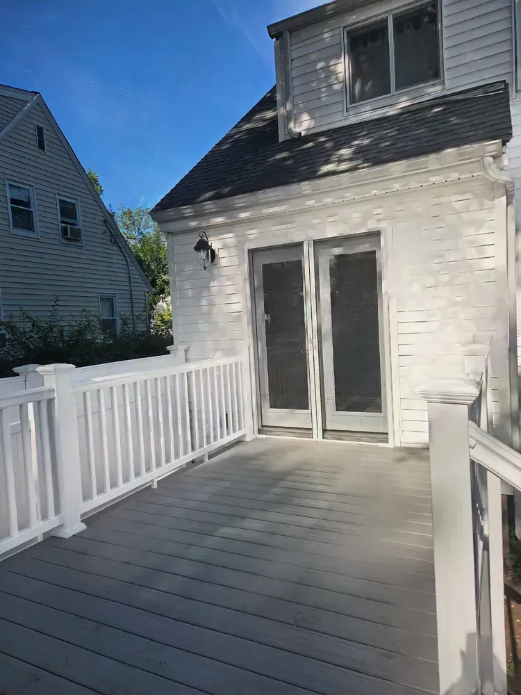 White house deck with gray floorboards, white railings, and sliding glass doors under a blue sky