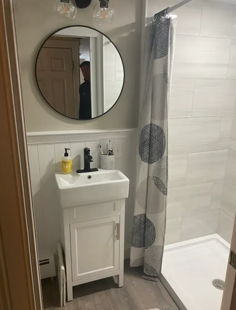 Small bathroom with white vanity, round mirror, black faucet, and shower curtain beside a shower.