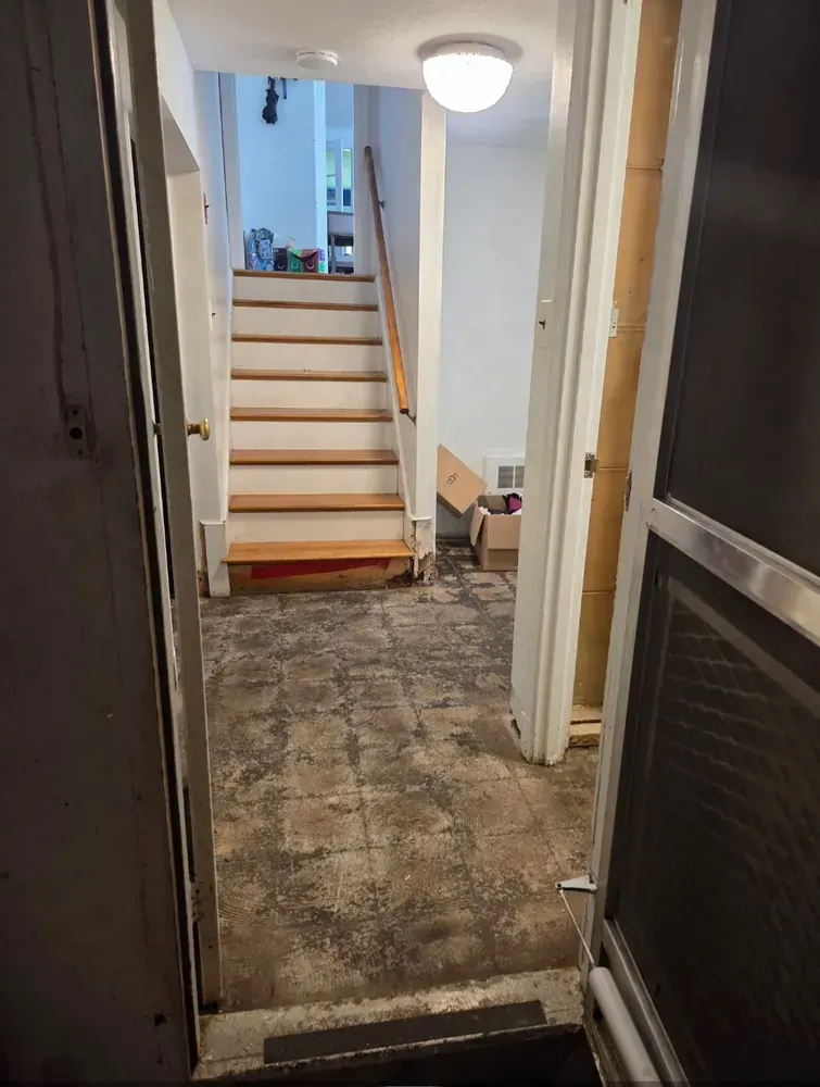 Dim hallway leading to a staircase, with worn flooring and an open door on the right.