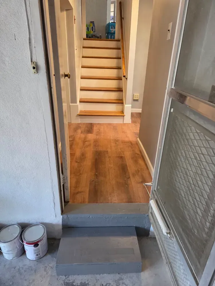 Front doorway with two steps up to a wood-floored hallway and staircase.