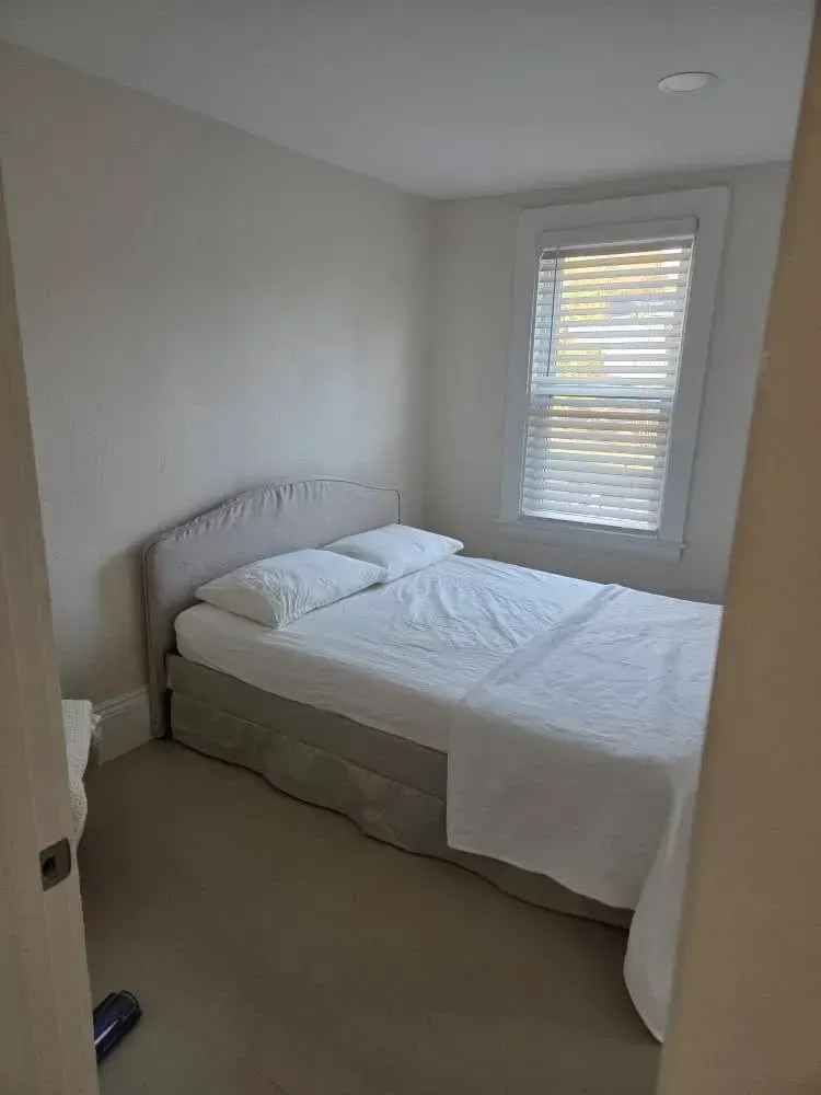 Small beige bedroom with an unmade bed and a window with blinds