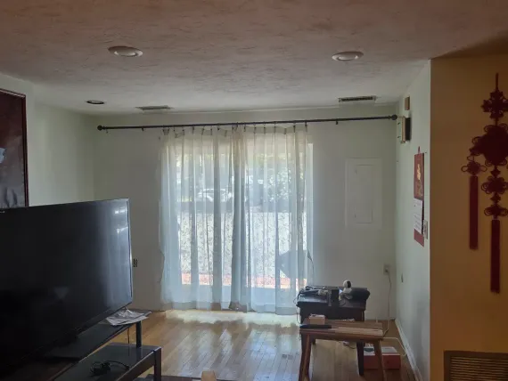 Living room with TV, sheer curtains, and sunlight streaming through sliding glass doors