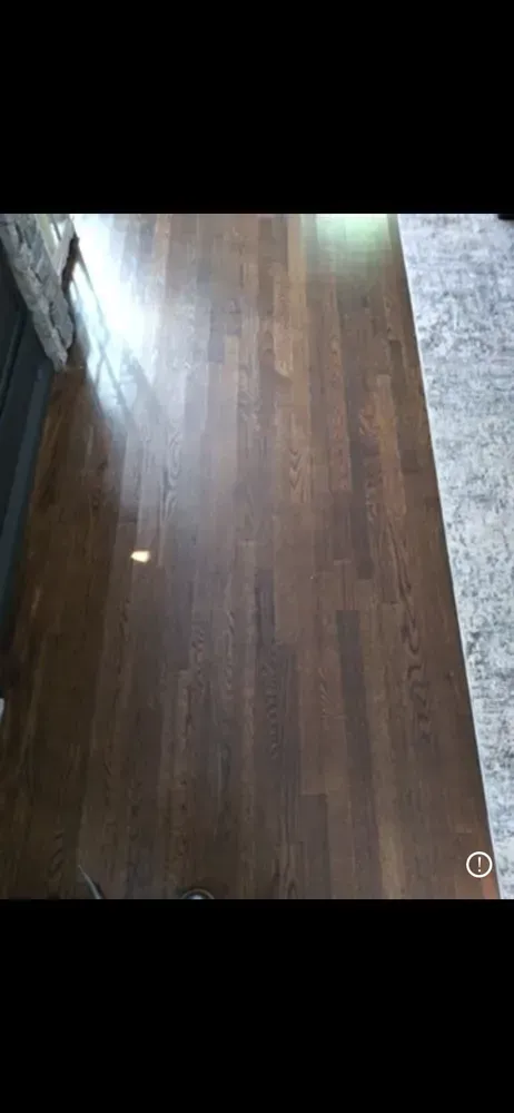 Wooden floor with sunlight reflecting near a gray carpet edge
