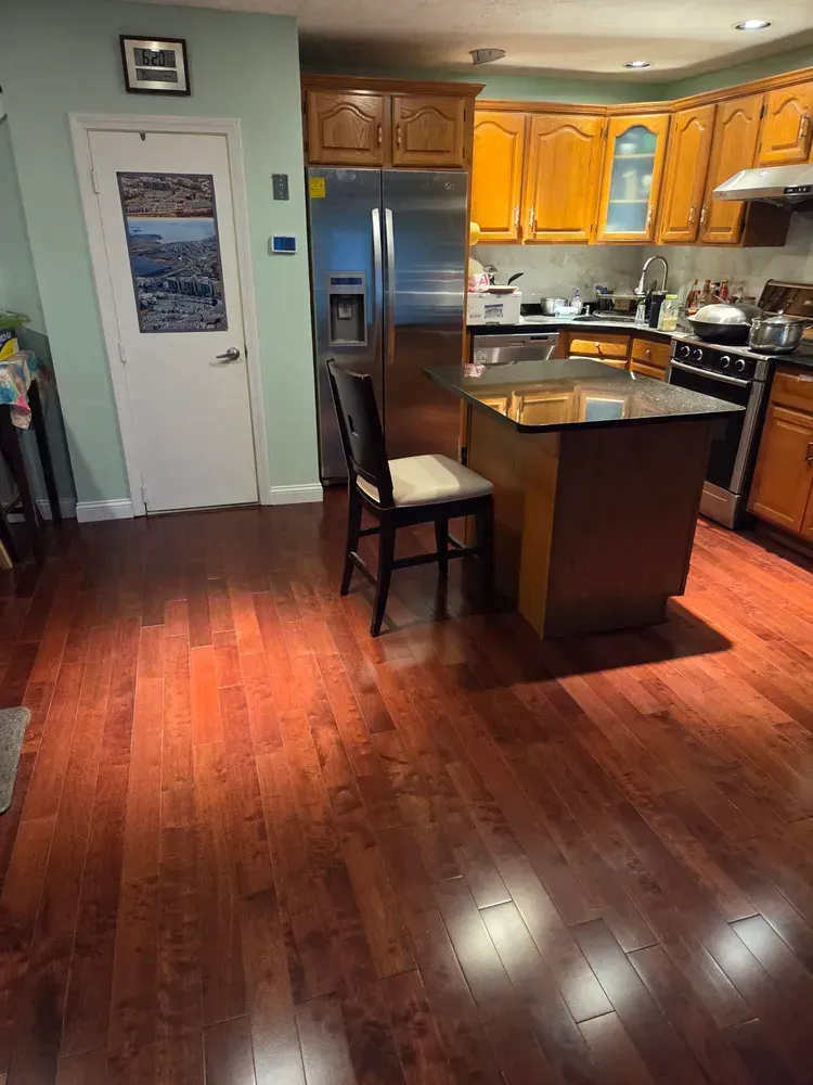 Kitchen with stainless fridge, wood cabinets, island, and hardwood floor, viewed from the living area