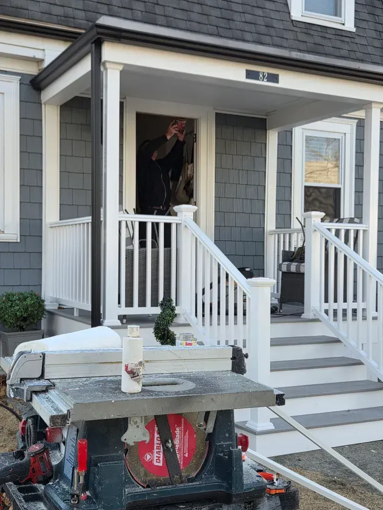 Person standing in a gray house doorway, with porch steps and a snow-covered table in front.