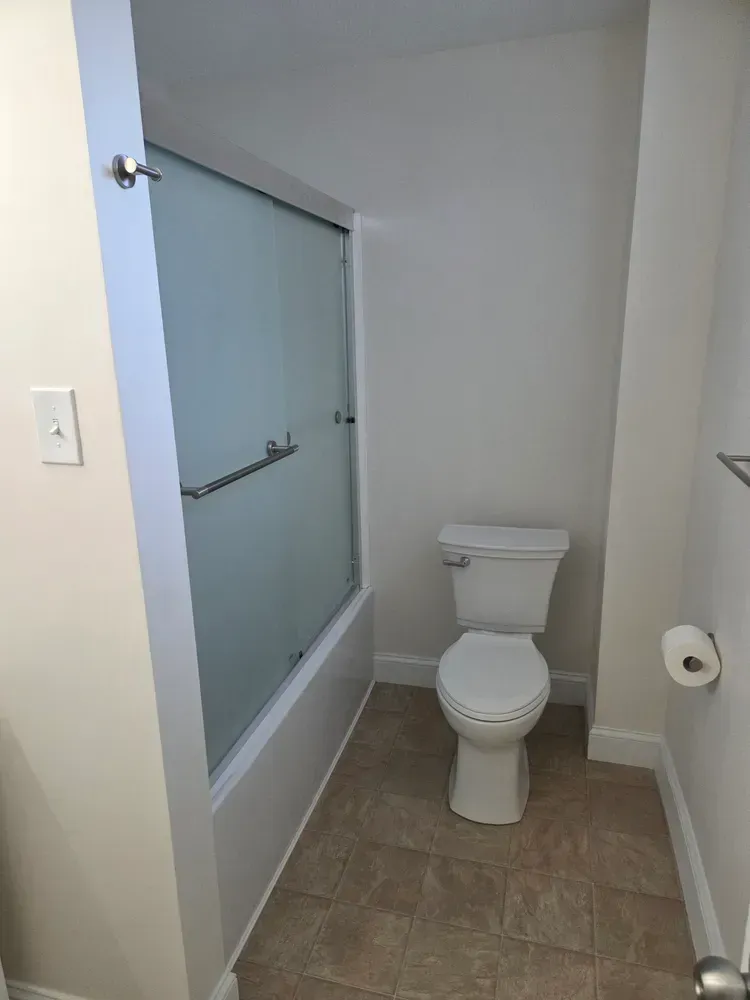 Small bathroom with toilet, frosted shower door, and tan tile floor