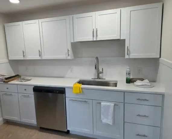 Modern kitchen with white cabinets, gray lower drawers, stainless dishwasher, sink, and countertop items