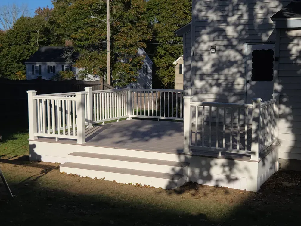 White wooden porch deck with railings beside a house in a sunny yard