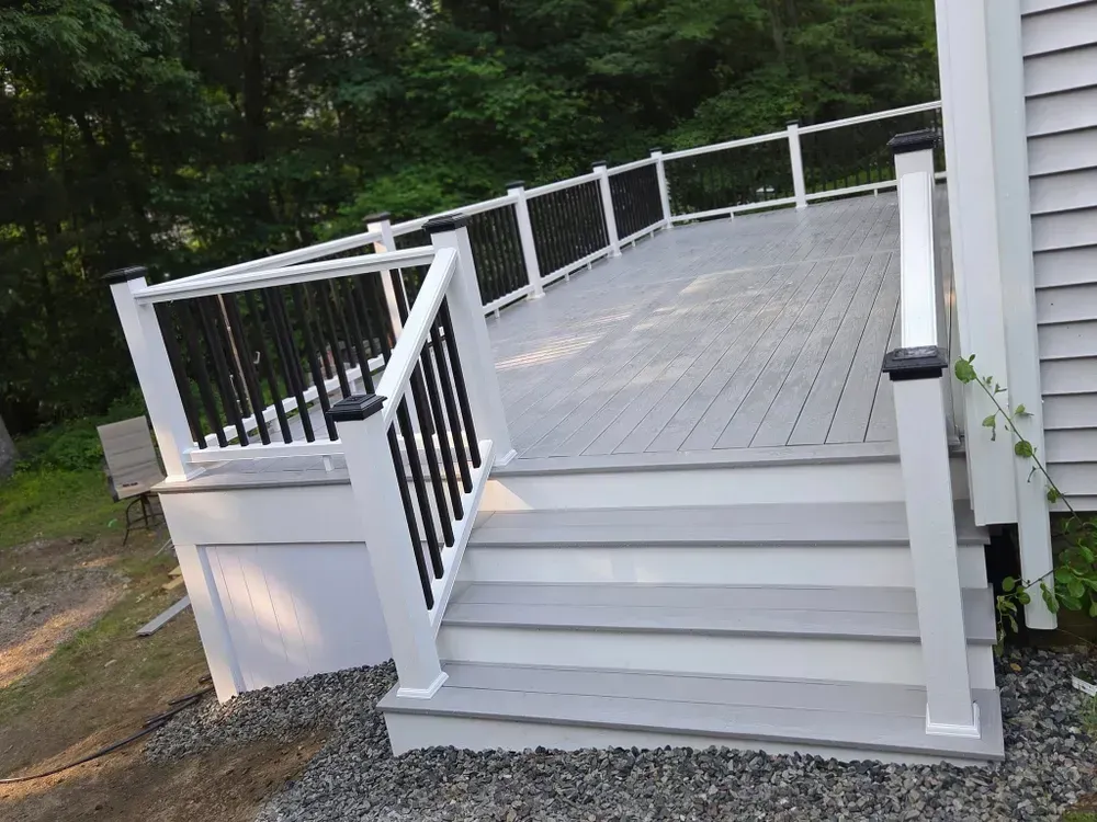 White accessible deck with steps, ramp-style railings, and gray flooring beside a wooded yard