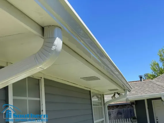 White gutter and downspout on a gray house under a clear blue sky