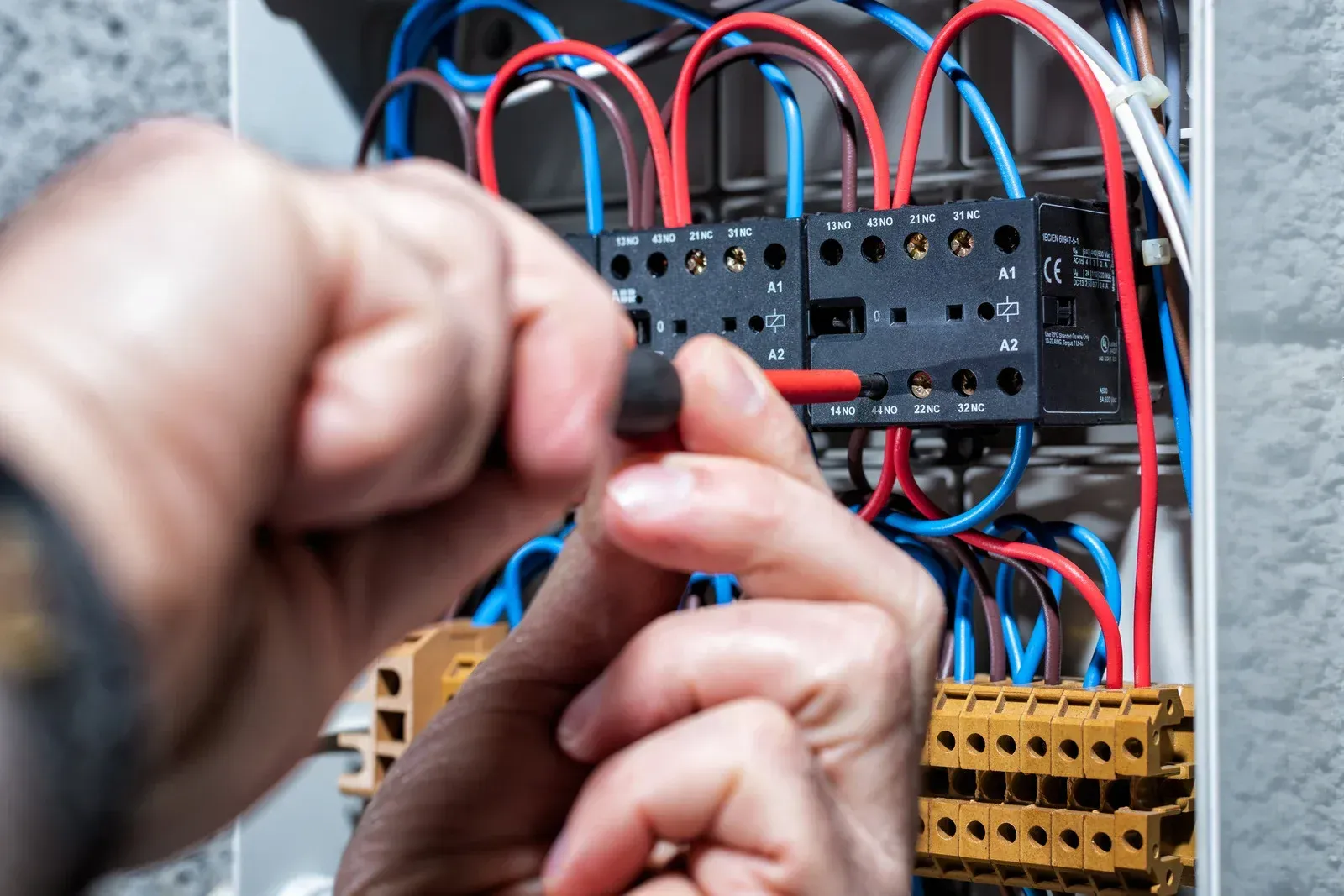 Hands of an electrician working on wiring inside an electrical panel; red, blue, and white wires.