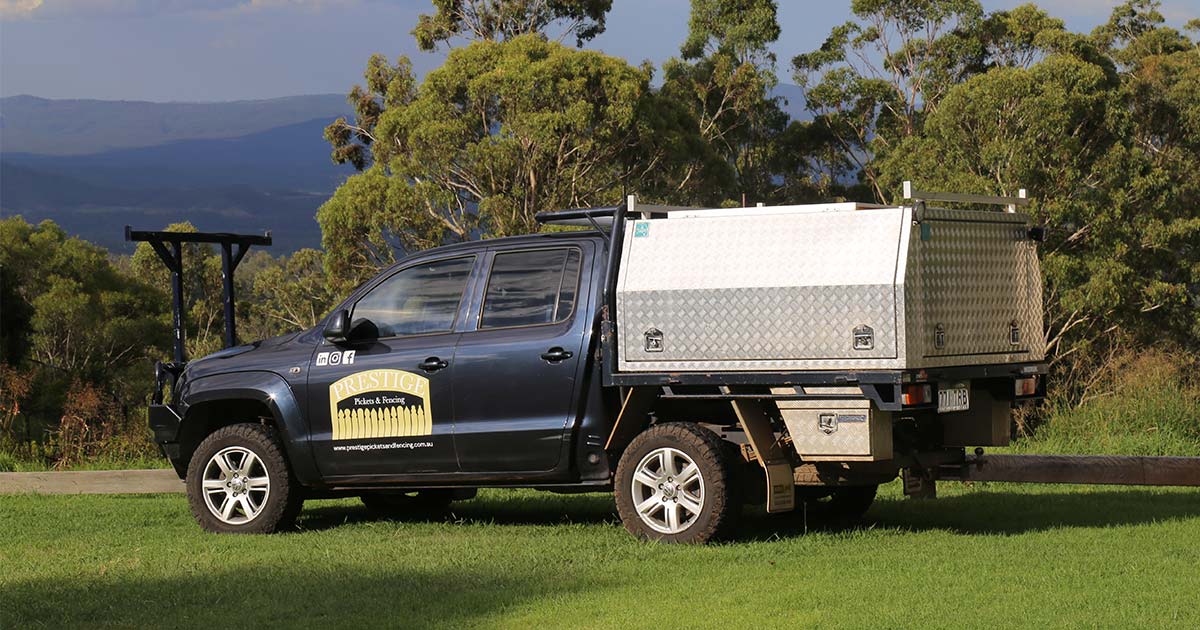 A ute is parked in a grassy field with trees in the background.
