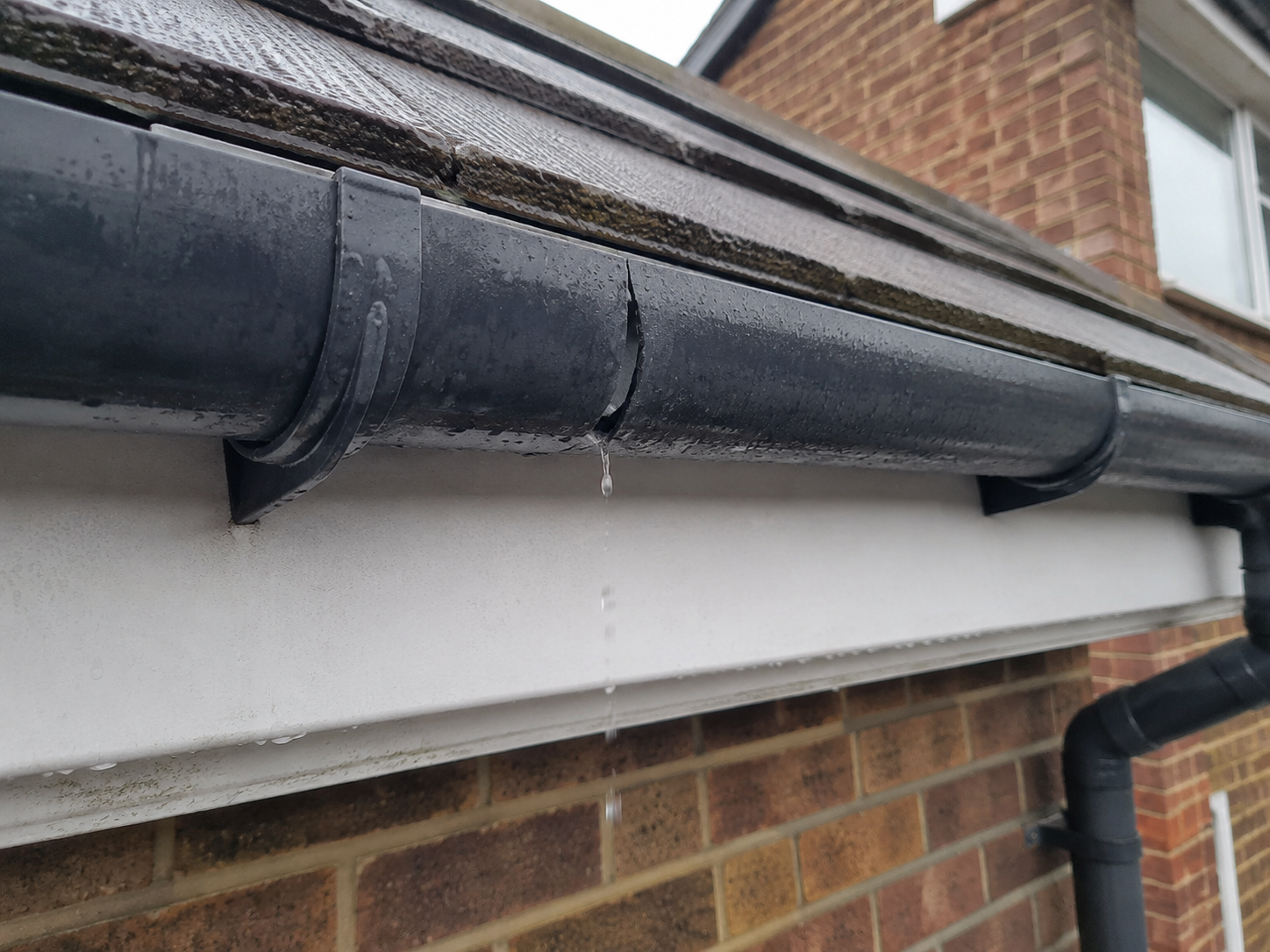 Cracked section of black uPVC guttering leaking rainwater