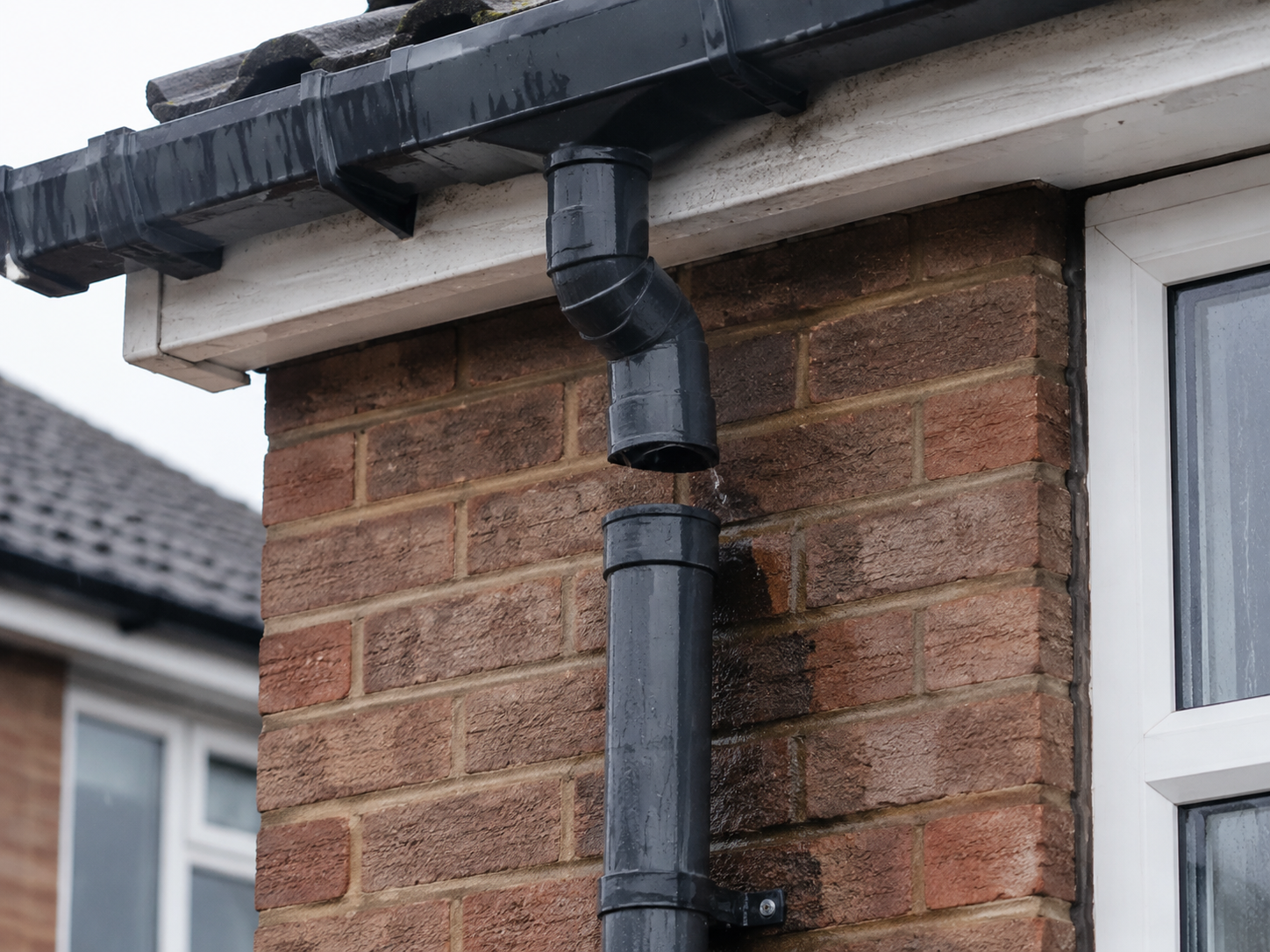 Disconnected black downpipe allowing rainwater to escape beside a brick wall