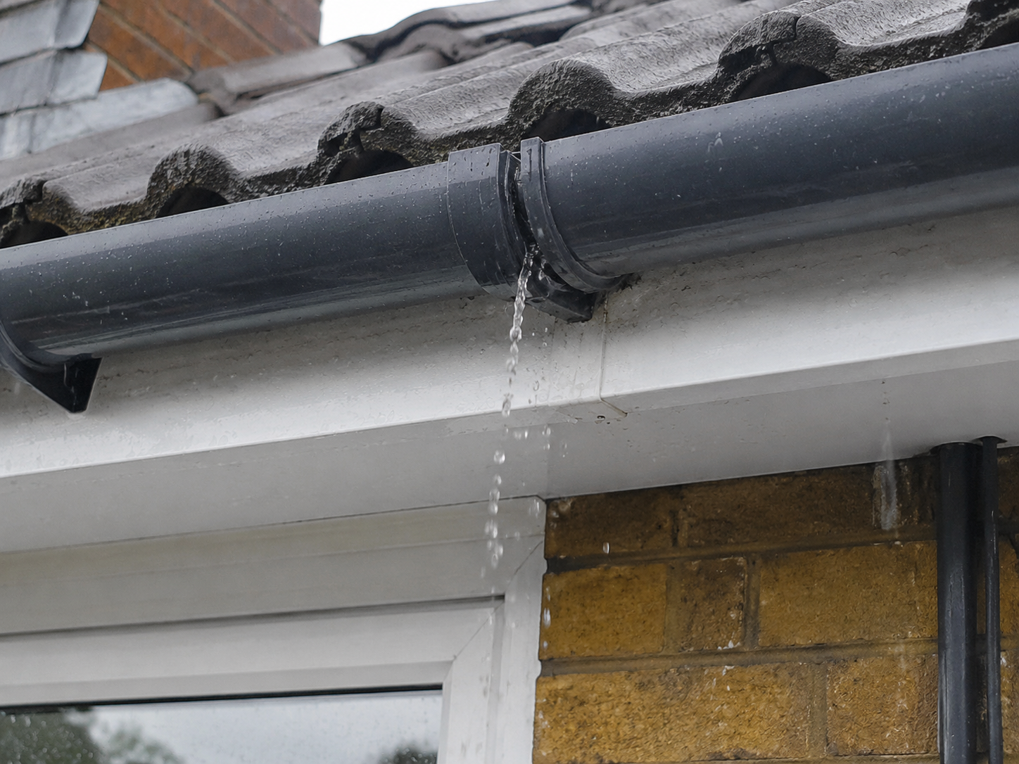 Rainwater leaking from a joint in black uPVC guttering