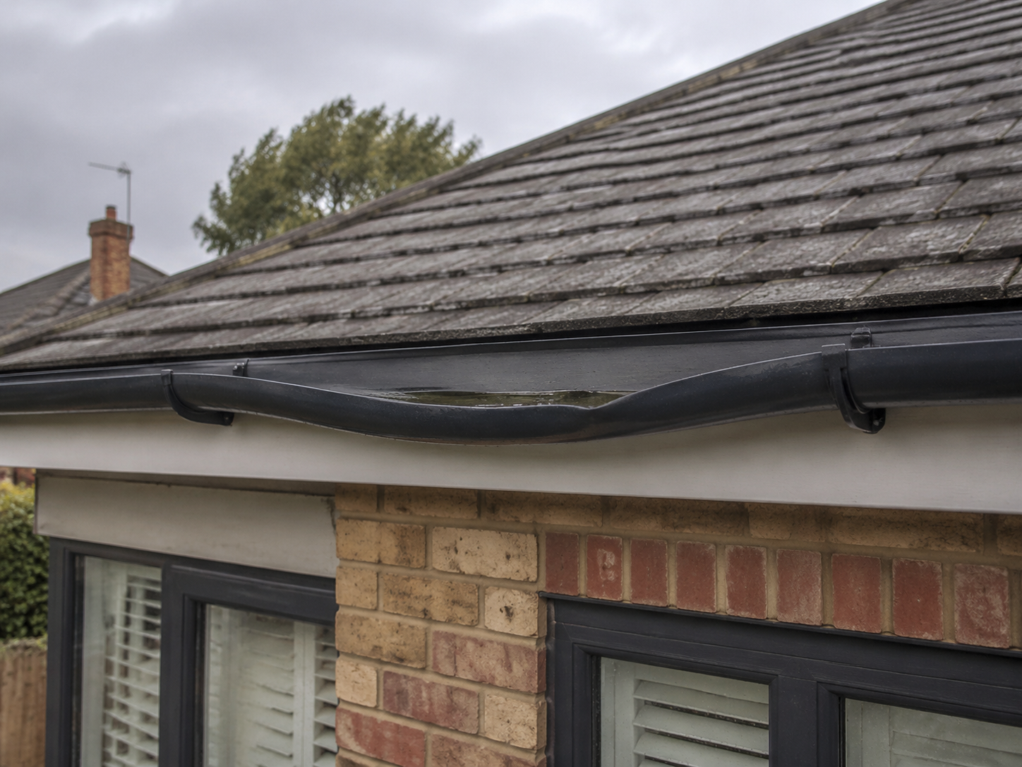 Sagging black guttering holding rainwater between support brackets