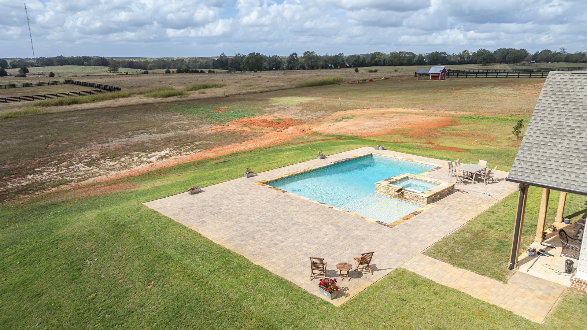 An aerial view of a large swimming pool in the middle of a lush green field.