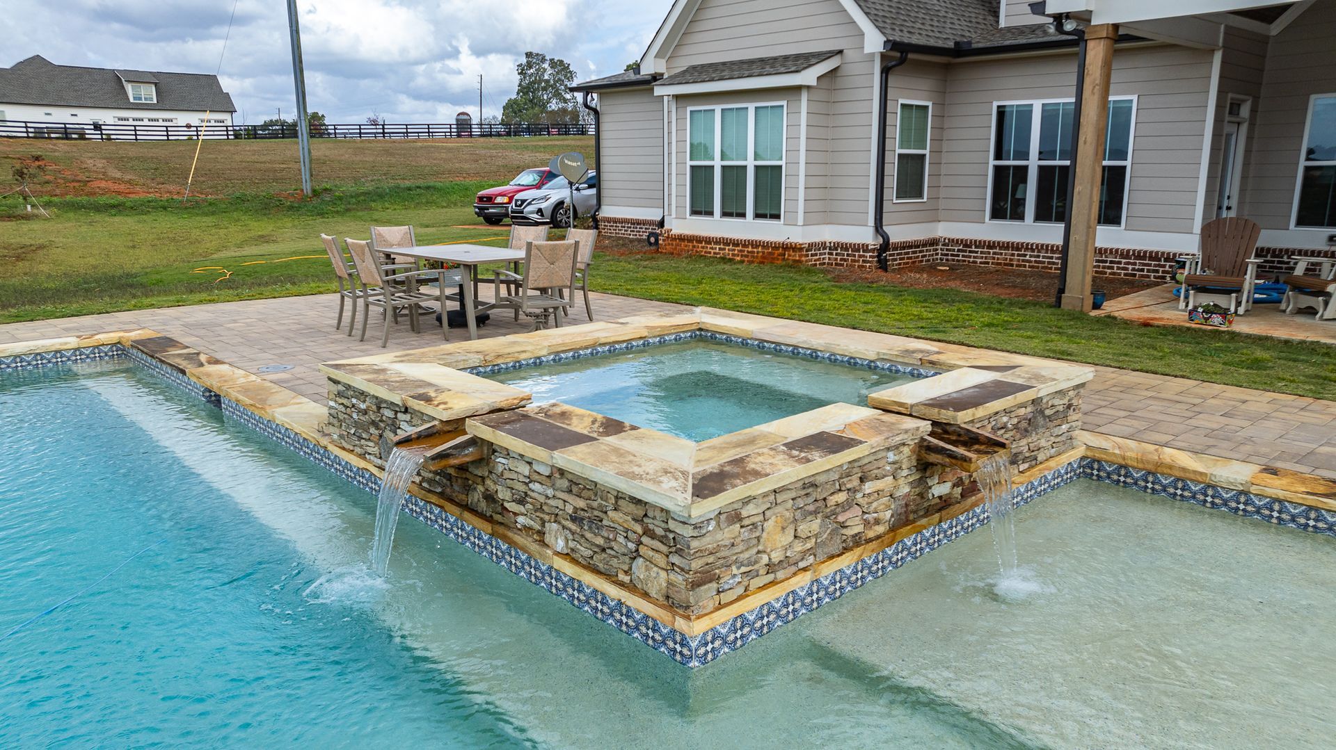 A large swimming pool with a hot tub and a table and chairs in front of a house.