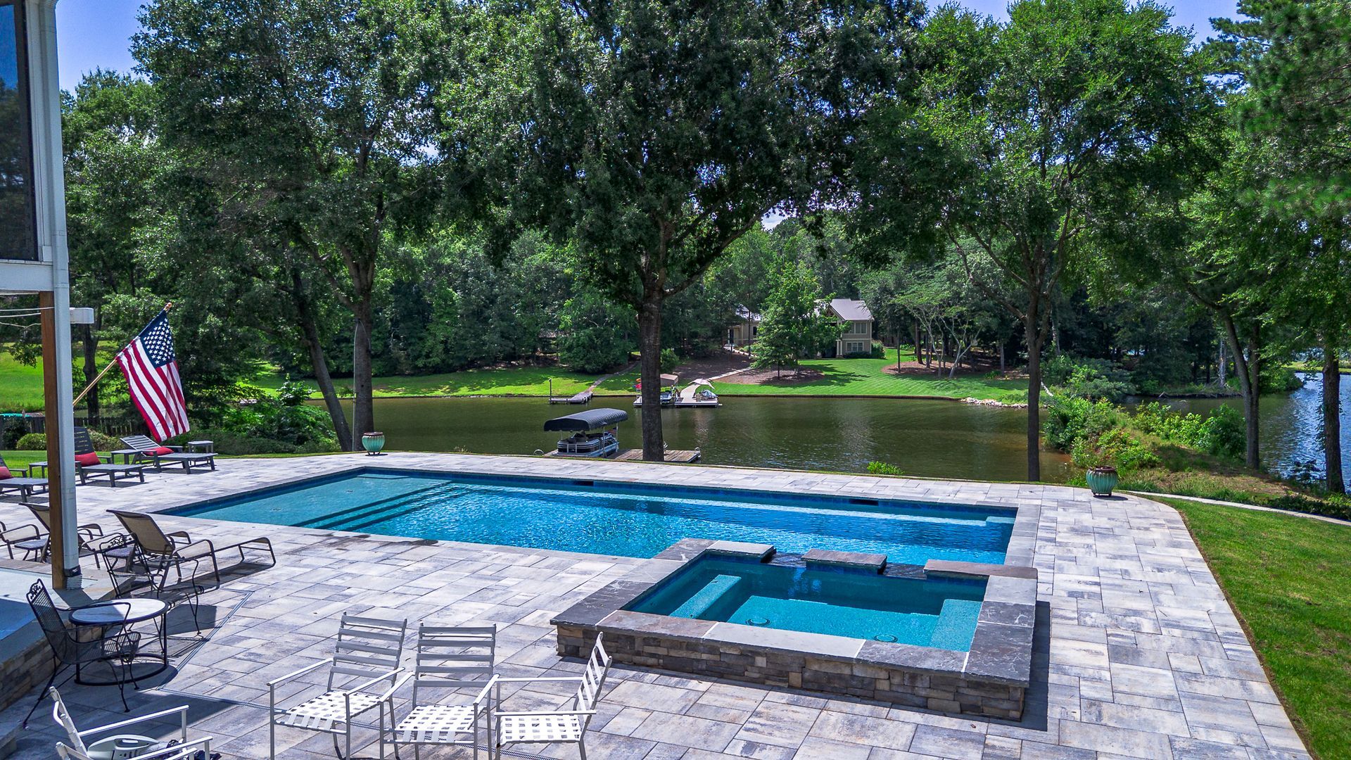 Backyard pool and spa overlooking a lake, with patio furniture and an American flag.