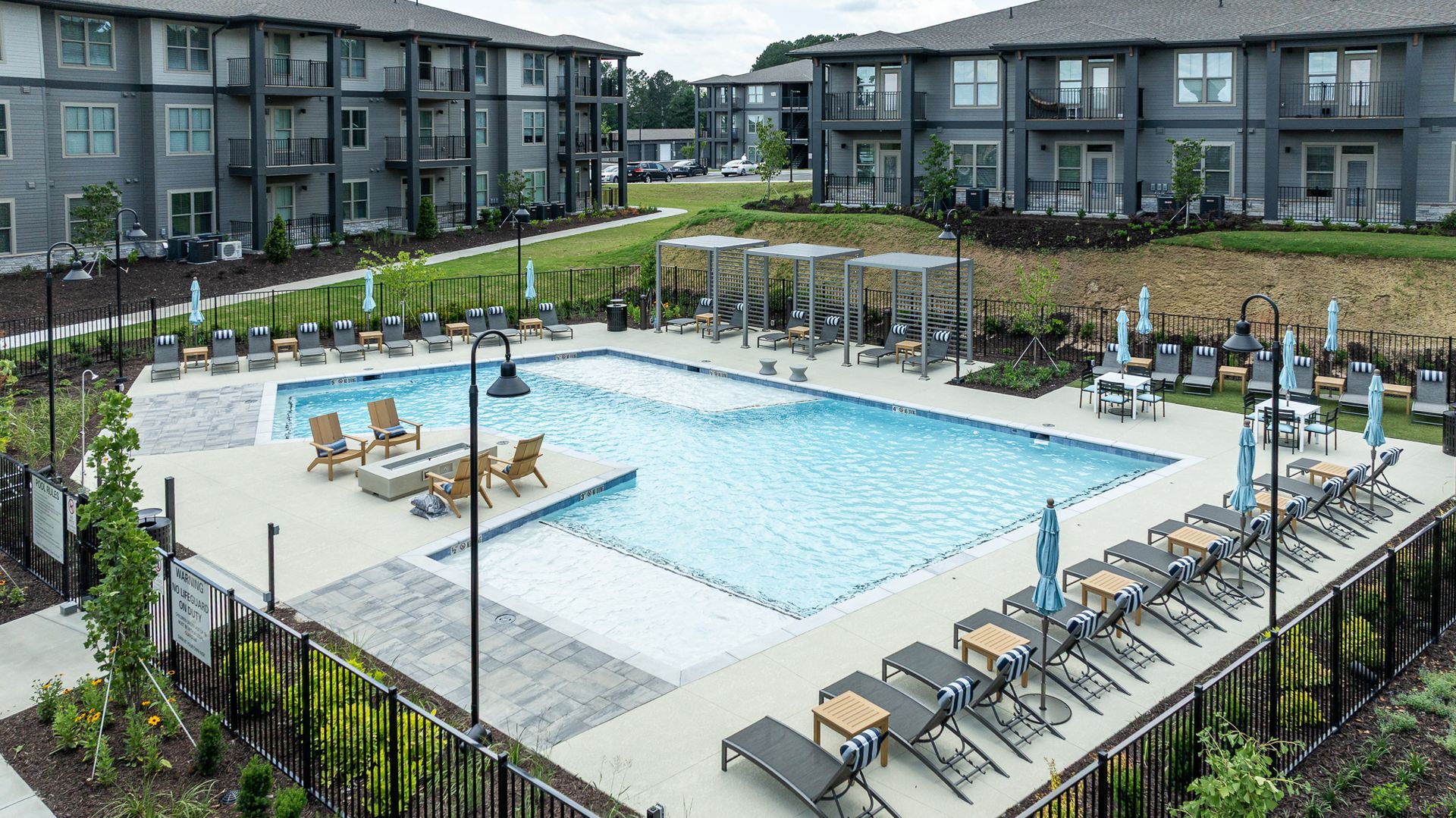 Apartment complex swimming pool with lounge chairs and umbrellas surrounded by multi-story buildings.