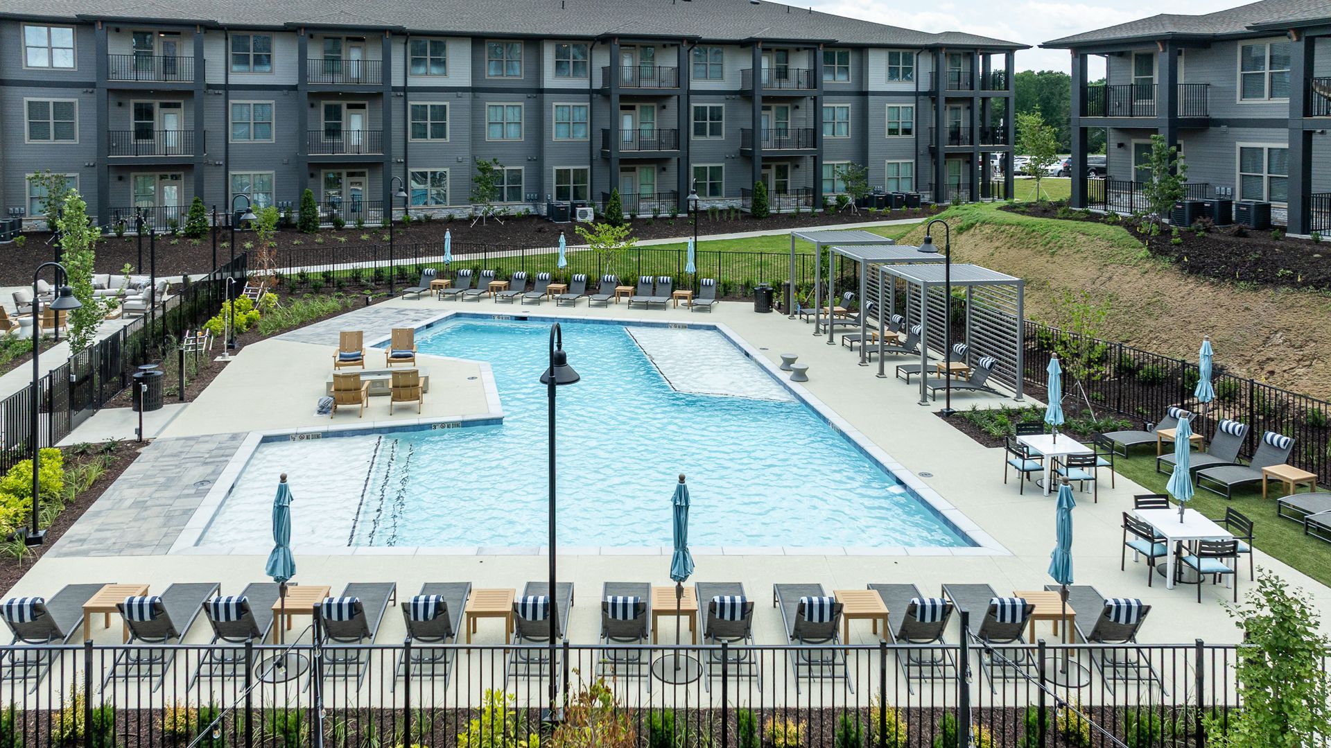 Apartment complex pool courtyard with lounge chairs, umbrellas, and surrounding buildings