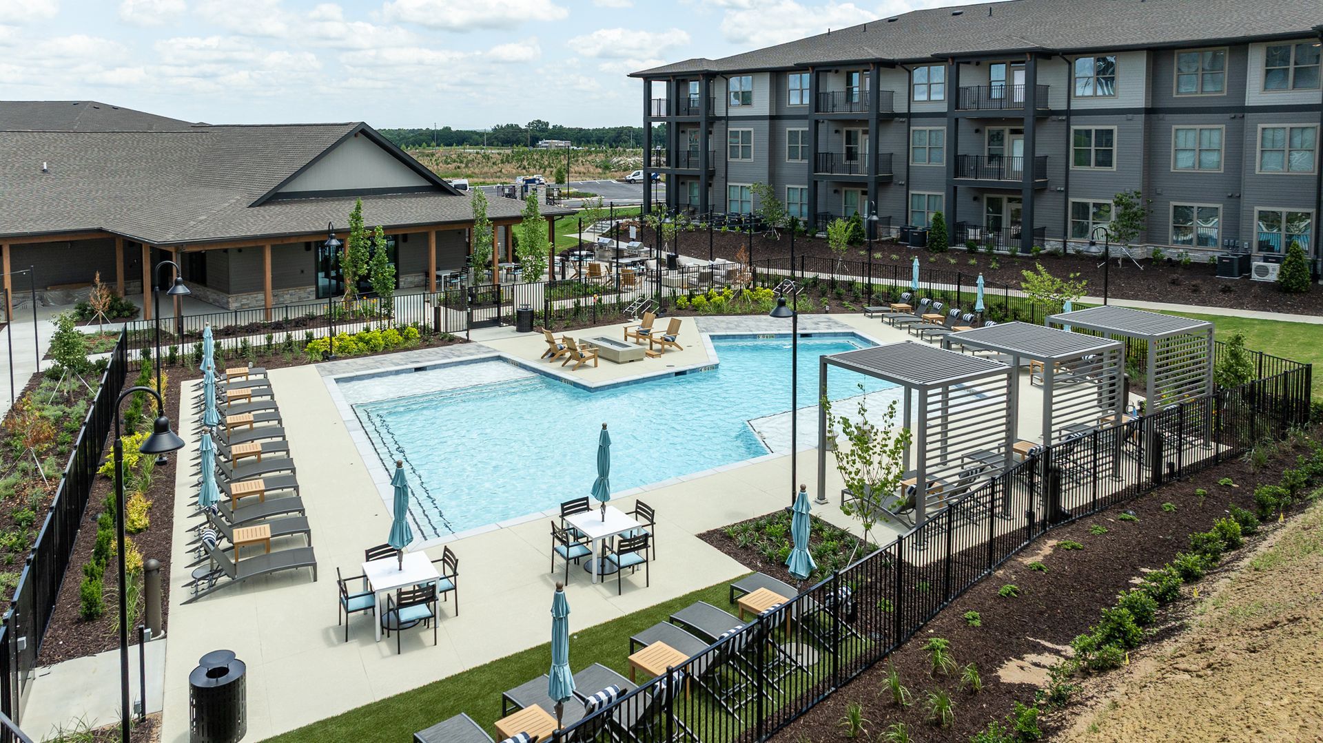 Outdoor resort pool with lounge chairs, pergola seating, and apartment buildings nearby