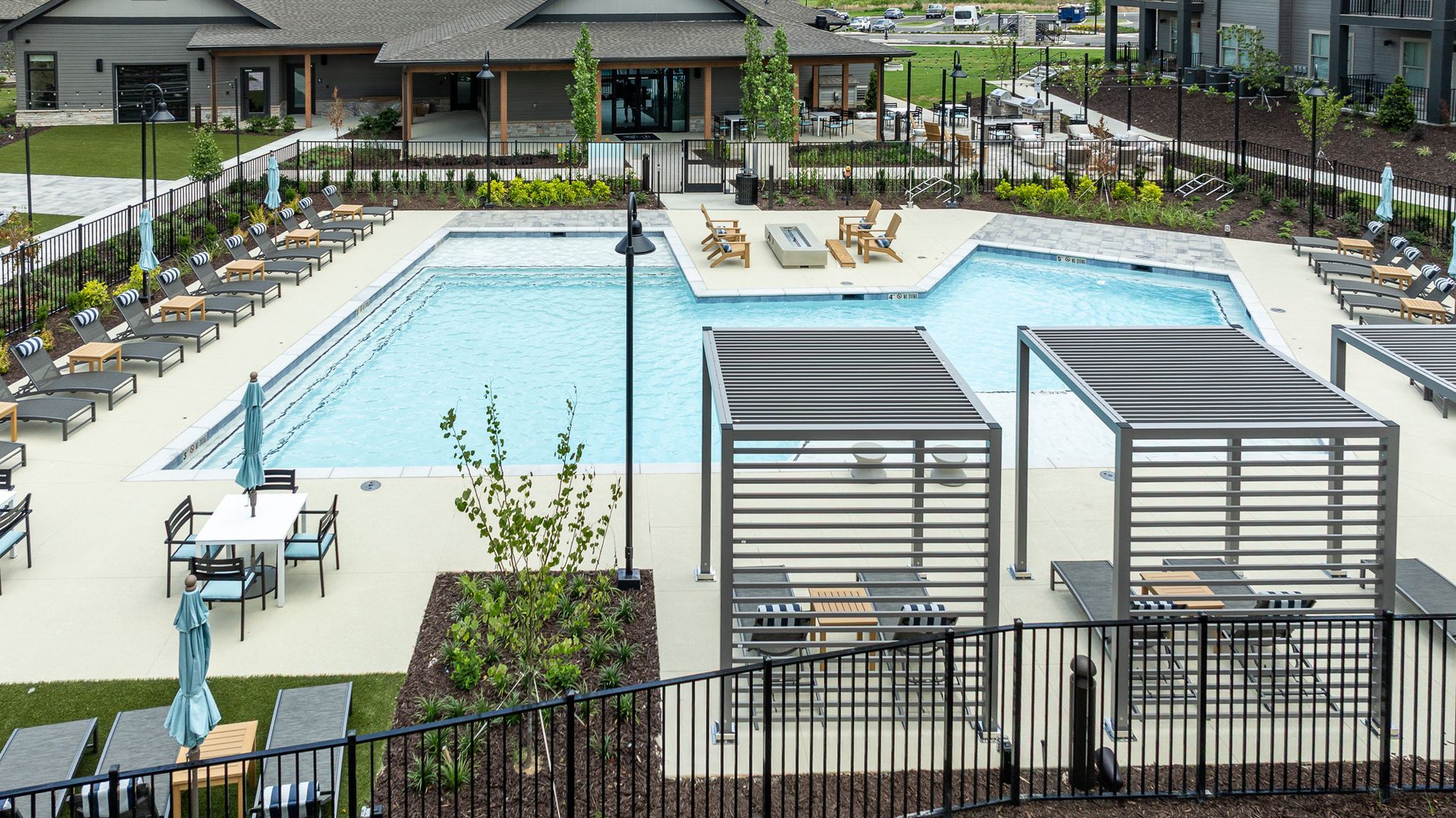 Outdoor apartment pool with lounge chairs, cabanas, and black metal fencing under a gray sky