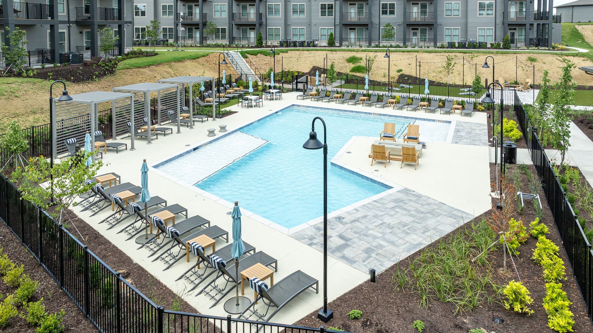 Outdoor apartment pool with blue water, lounge chairs, and white cabanas in a landscaped courtyard