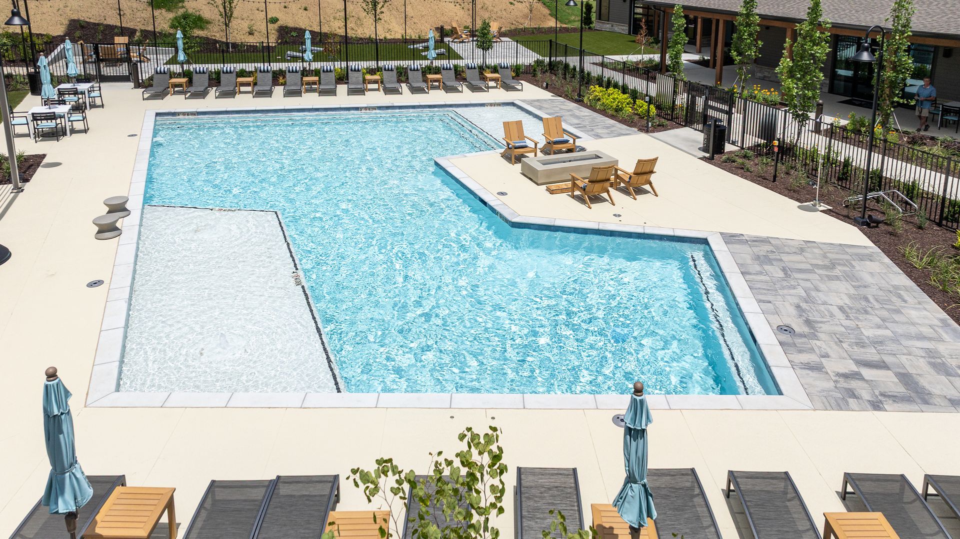 Outdoor swimming pool with lounge chairs, umbrellas, and a shallow ledge under bright sunlight.