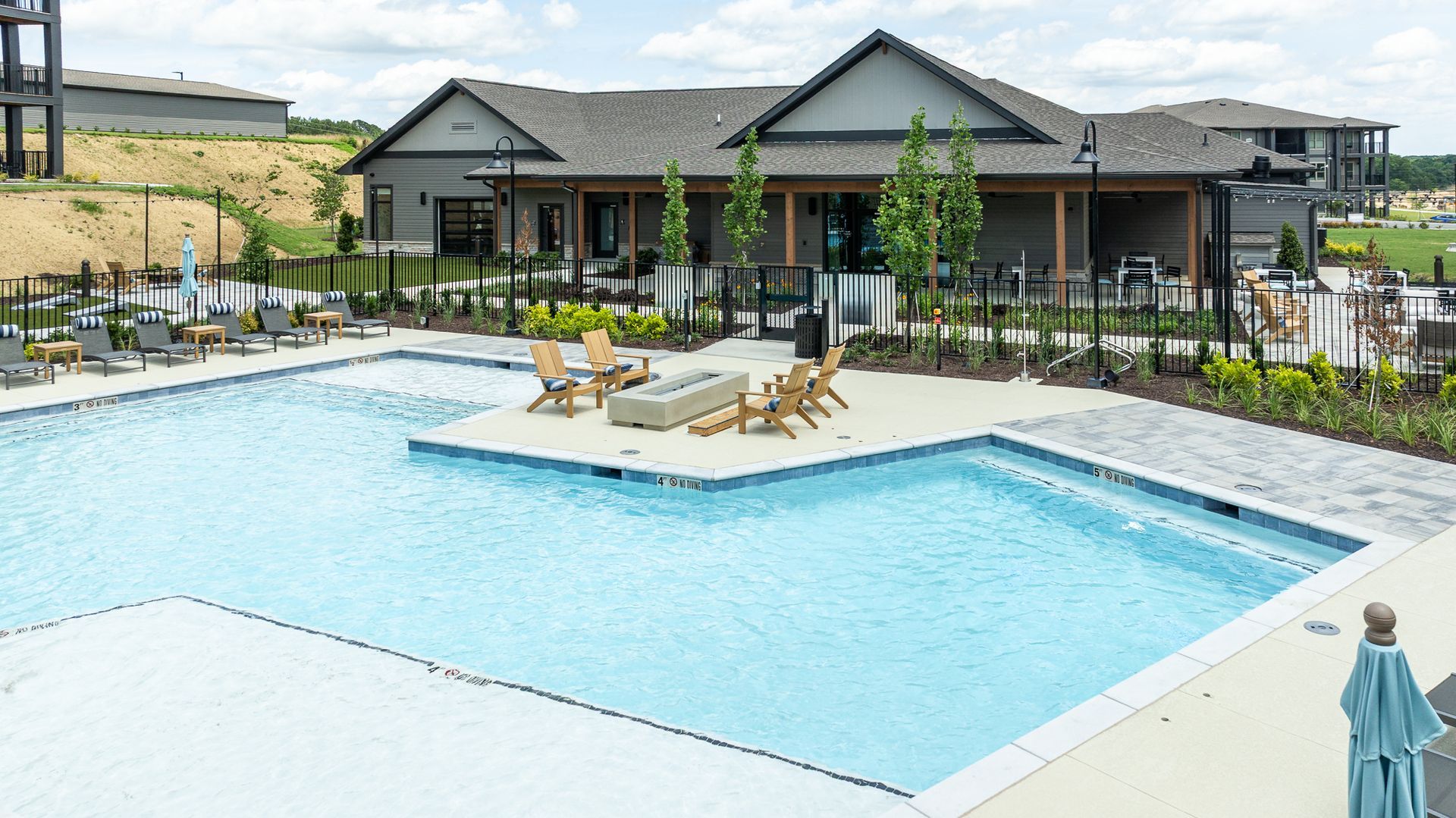 Outdoor resort pool with lounge chairs and a central sun shelf beside a clubhouse building.