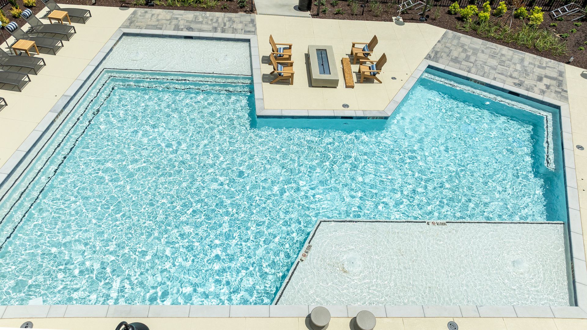 A bright blue swimming pool with a small sun deck, lounge chairs, and surrounding stone paving.