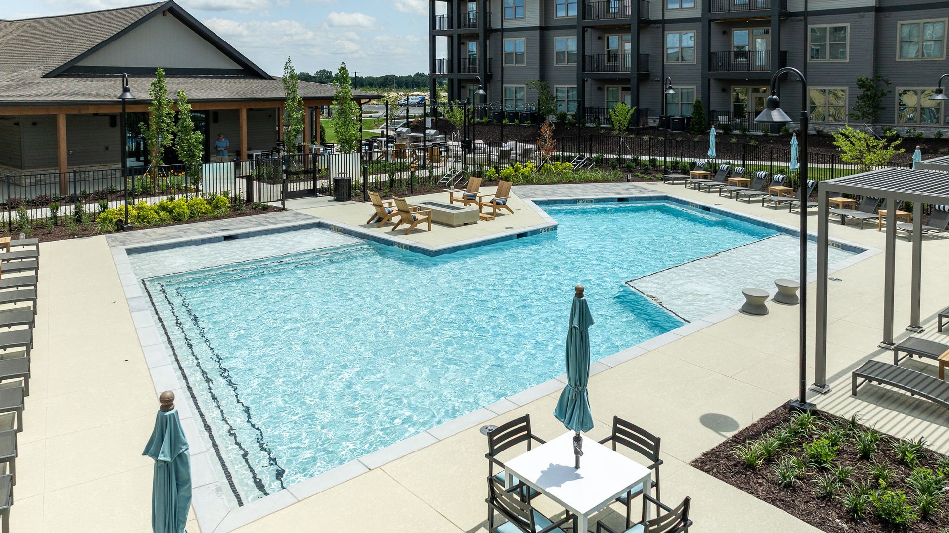 Outdoor apartment pool with lounge chairs, umbrellas, and landscaped seating area.