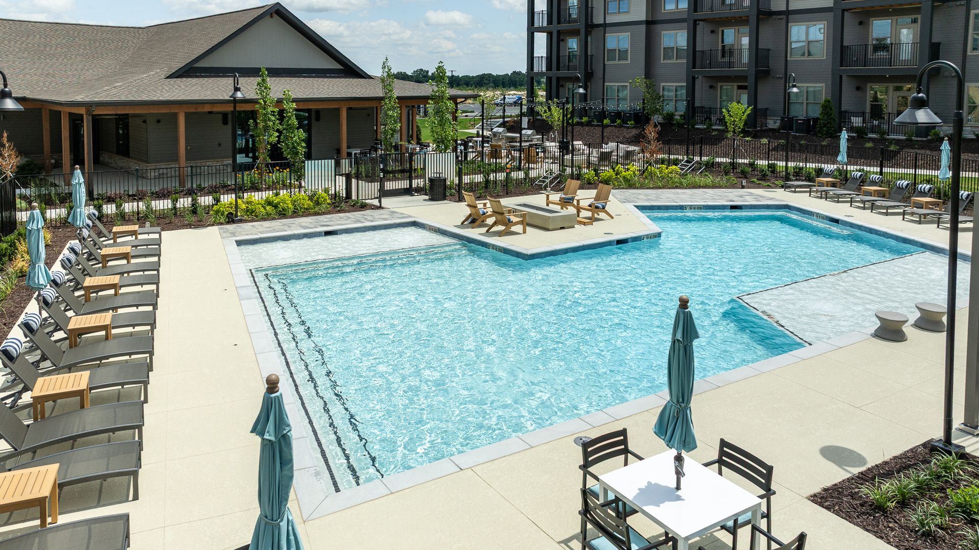Outdoor apartment pool with lounge chairs, umbrellas, and a hot tub on a sunny day