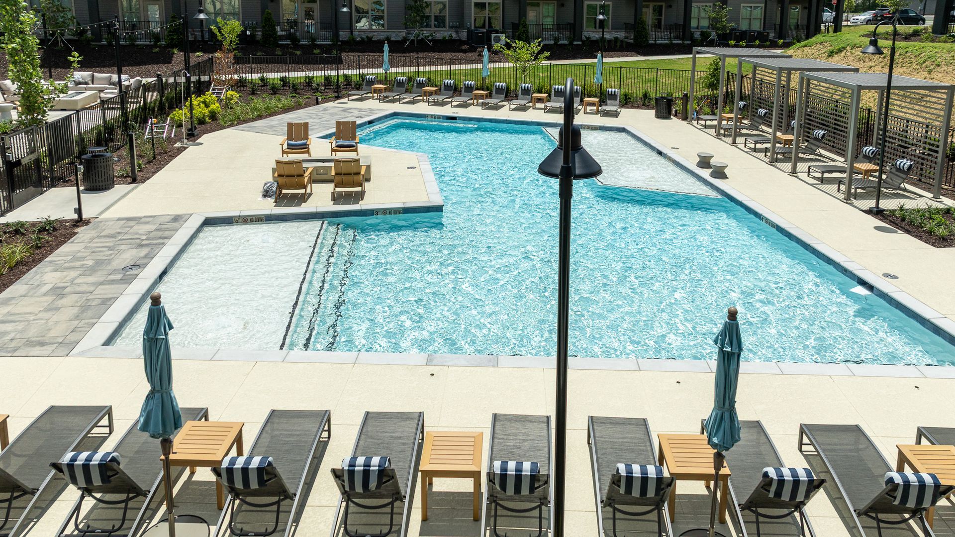 Outdoor resort pool with lounge chairs, umbrellas, and a central water feature on a sunny day