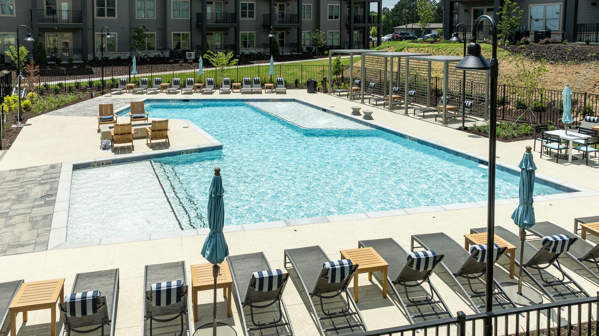 Outdoor apartment pool with lounge chairs, umbrellas, and clear blue water on a sunny day