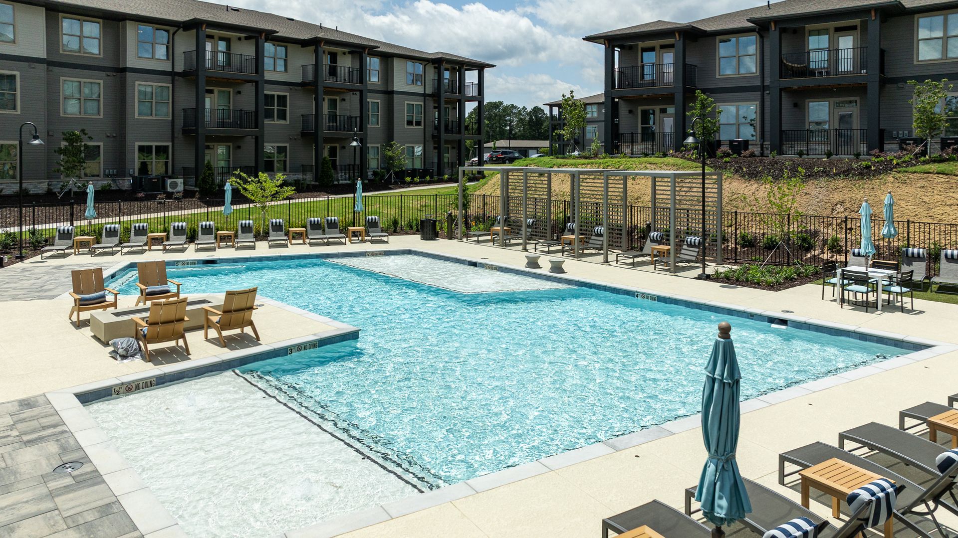 Apartment complex pool courtyard with lounge chairs and umbrellas under a cloudy sky