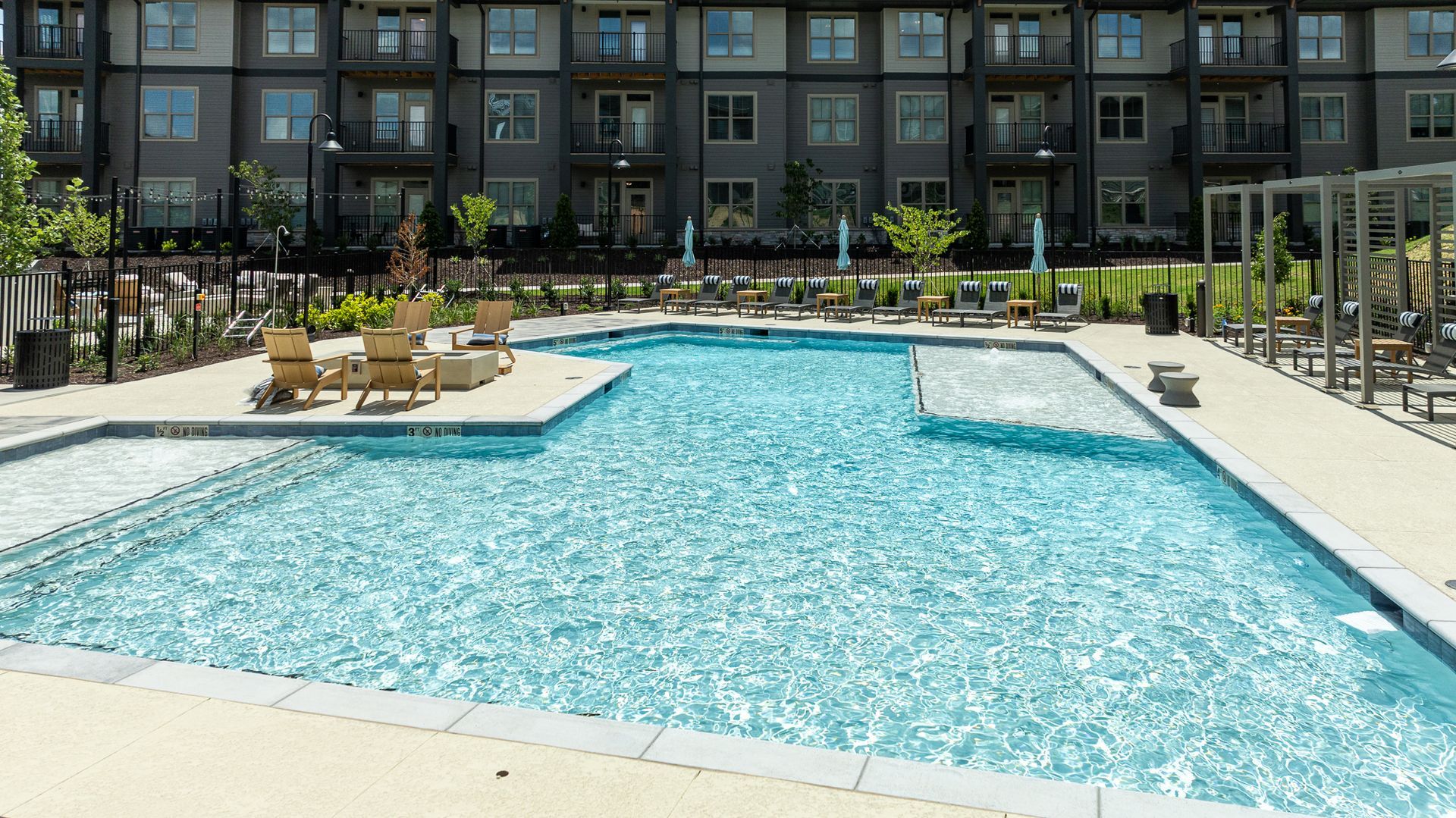 Outdoor apartment pool with turquoise water, lounge chairs, and surrounding modern buildings
