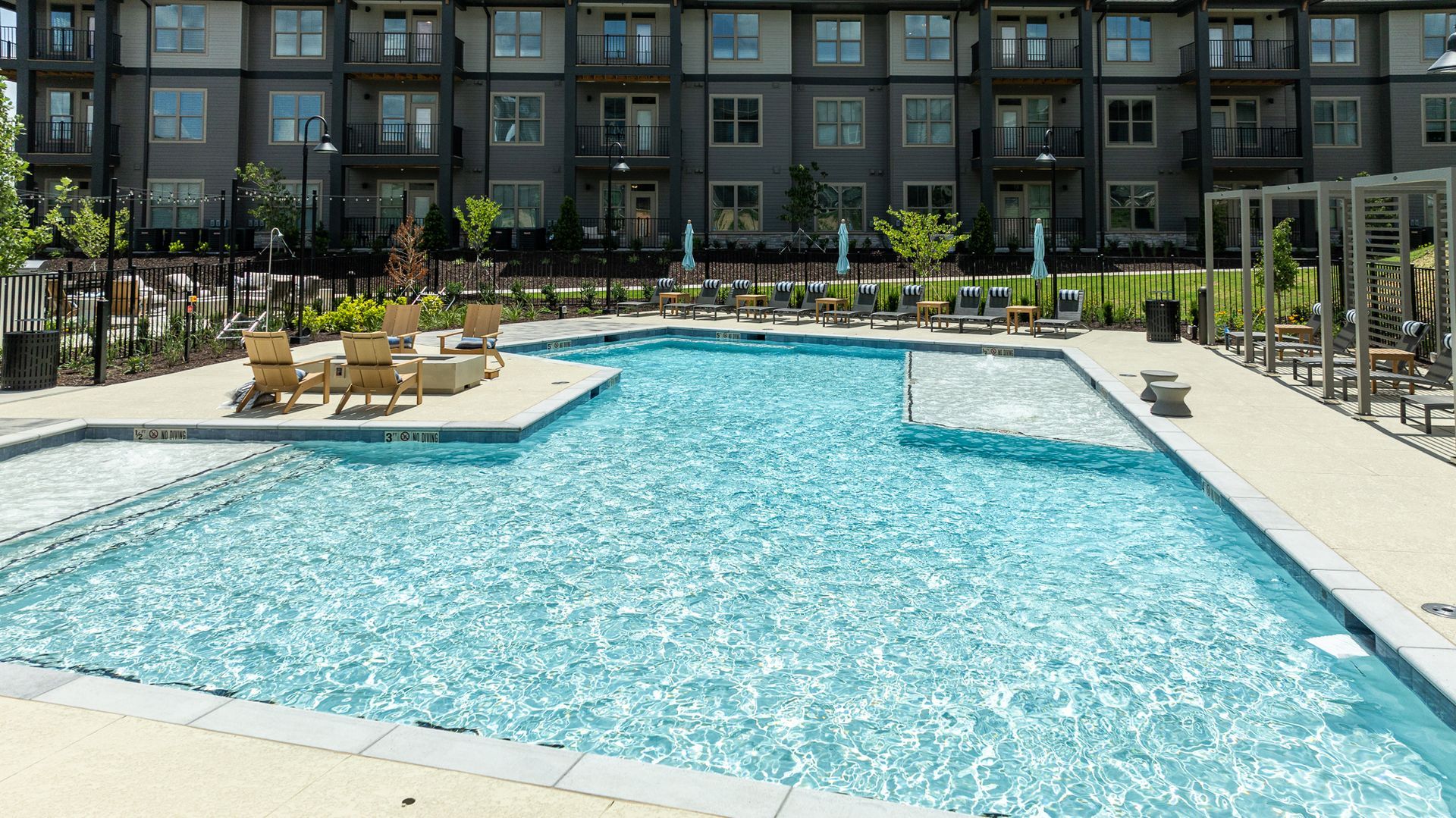 Outdoor apartment pool with turquoise water, lounge chairs, and a modern building courtyard backdrop