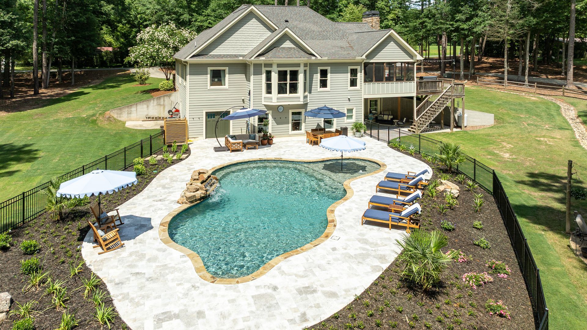 Backyard home with freeform pool, stone patio, lounge chairs, and landscaped garden