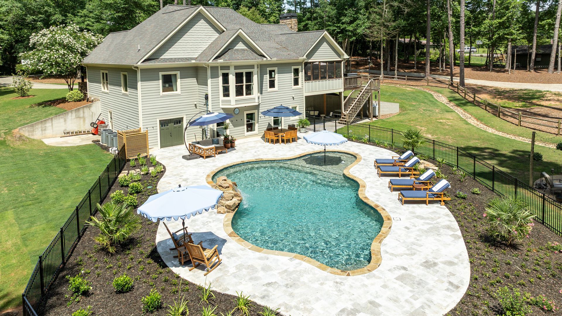 Backyard pool with stone patio, lounge chairs, umbrella, and a house in the background