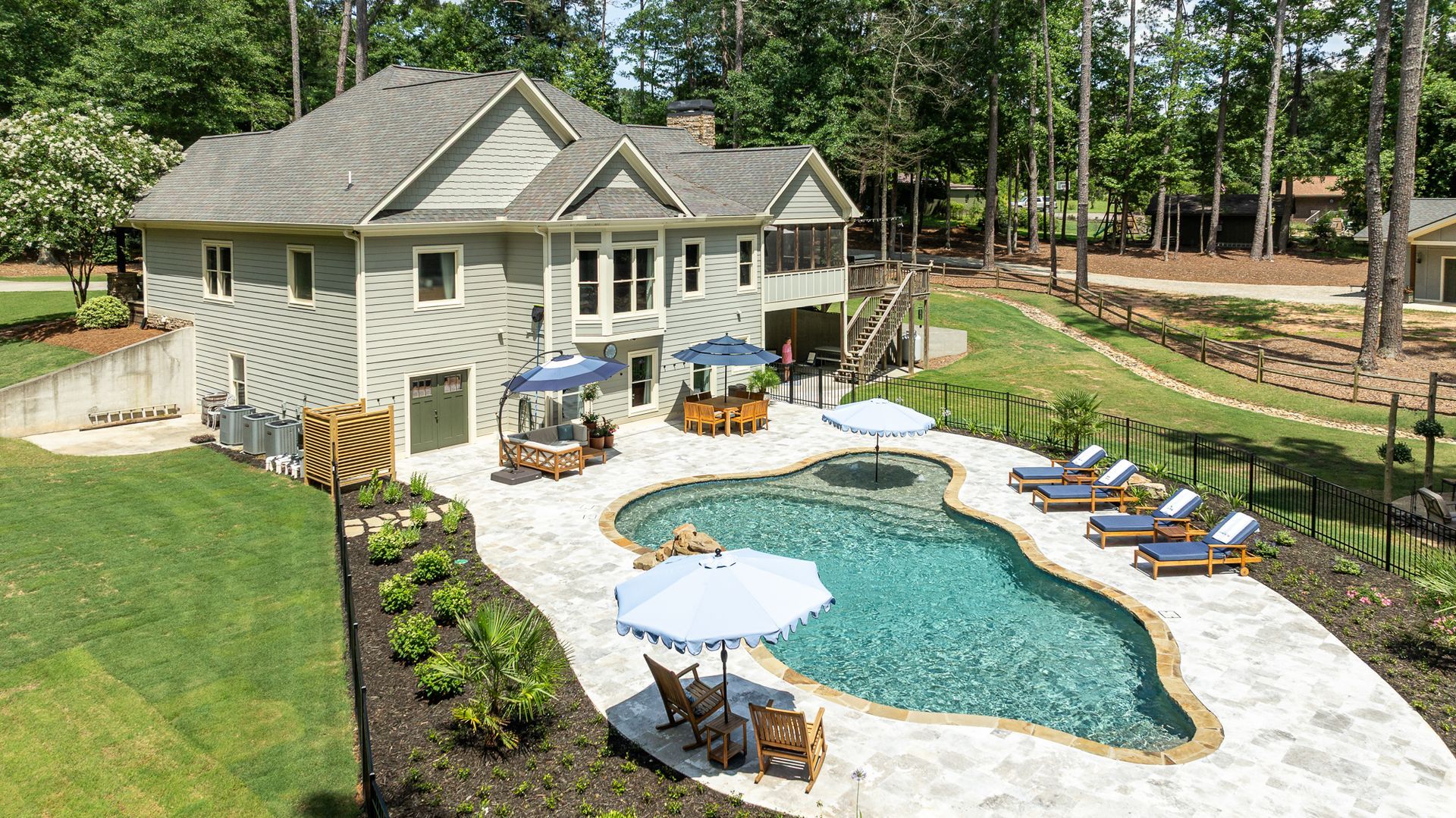 Backyard with kidney-shaped pool, white stone patio, loungers, and a beige house surrounded by trees
