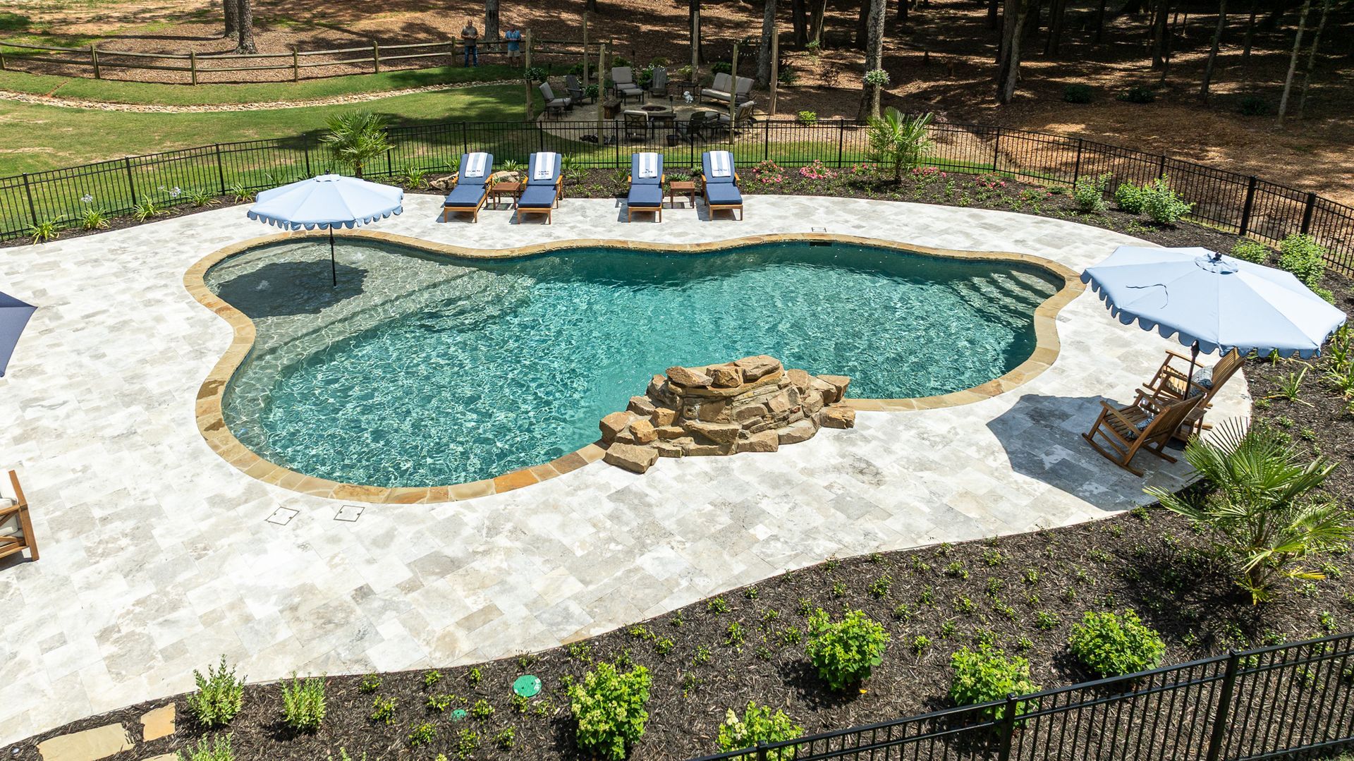 Curved backyard pool with stone deck, lounge chairs, and landscaping, viewed from above