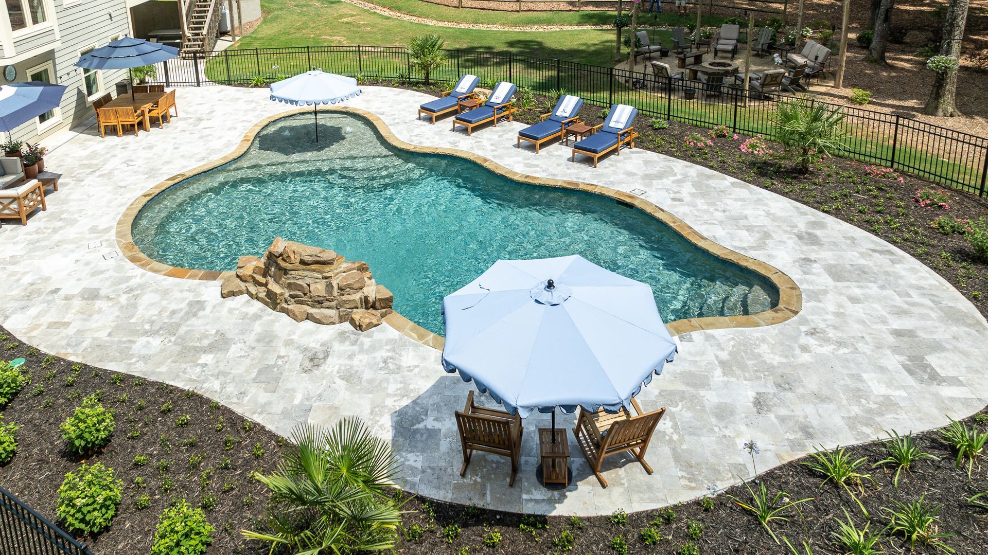 Backyard pool with light stone deck, lounge chairs, and a white patio umbrella.
