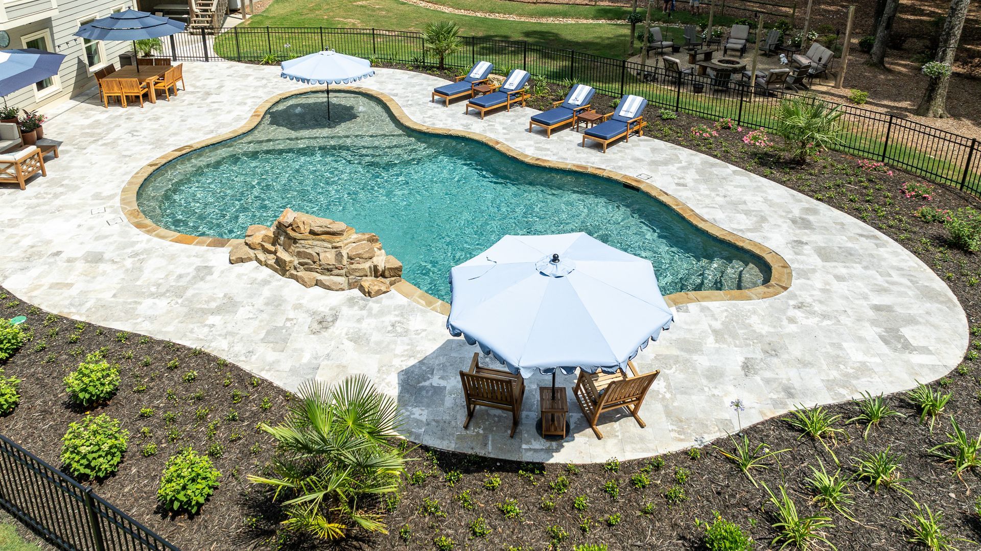 Backyard pool with white stone deck, blue lounge chairs, and patio umbrellas